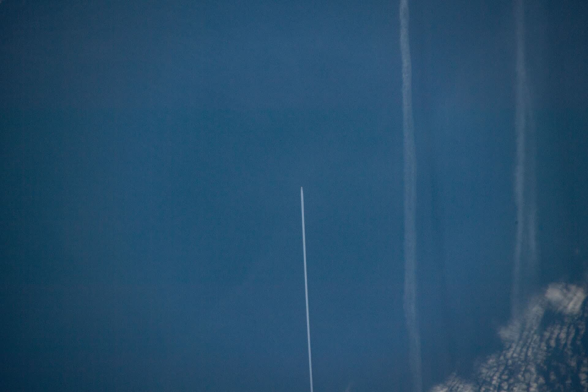 The white contrail of an airliner crossing the blue North Atlantic, seen from above