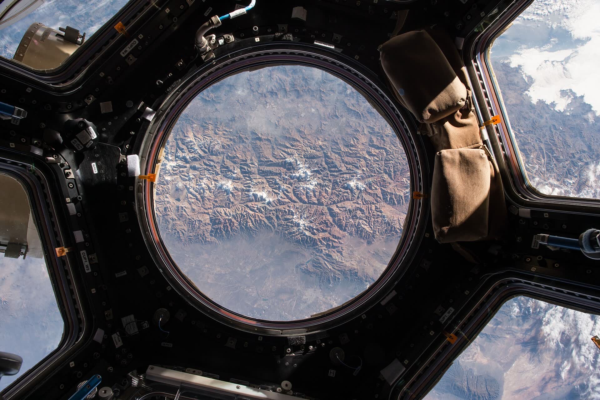 The round central window of the space station’s cupola, looking down on mountains and cloud