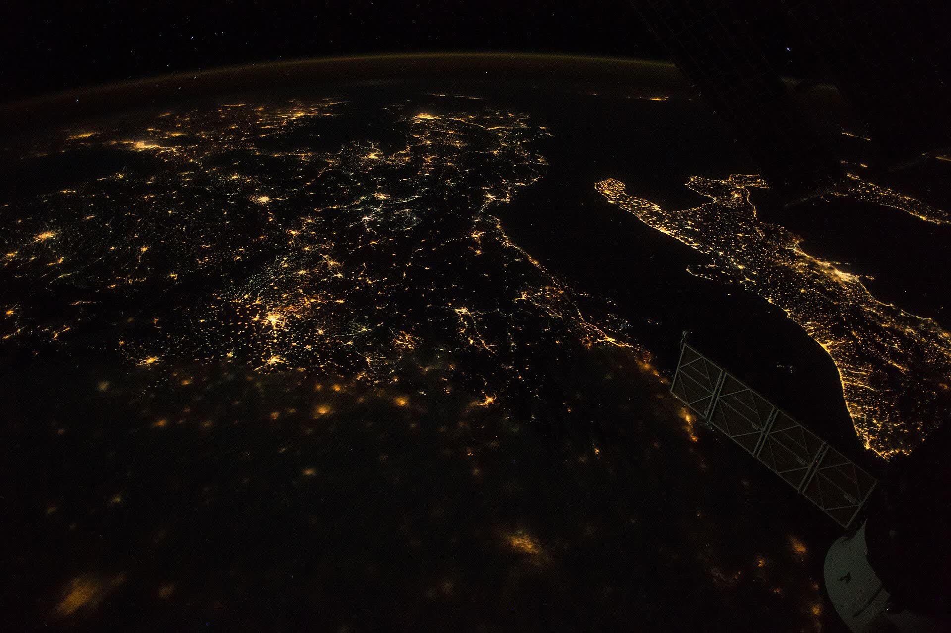 City lights across southern Europe at night, with the boot of Italy and a solar panel of the space station in view