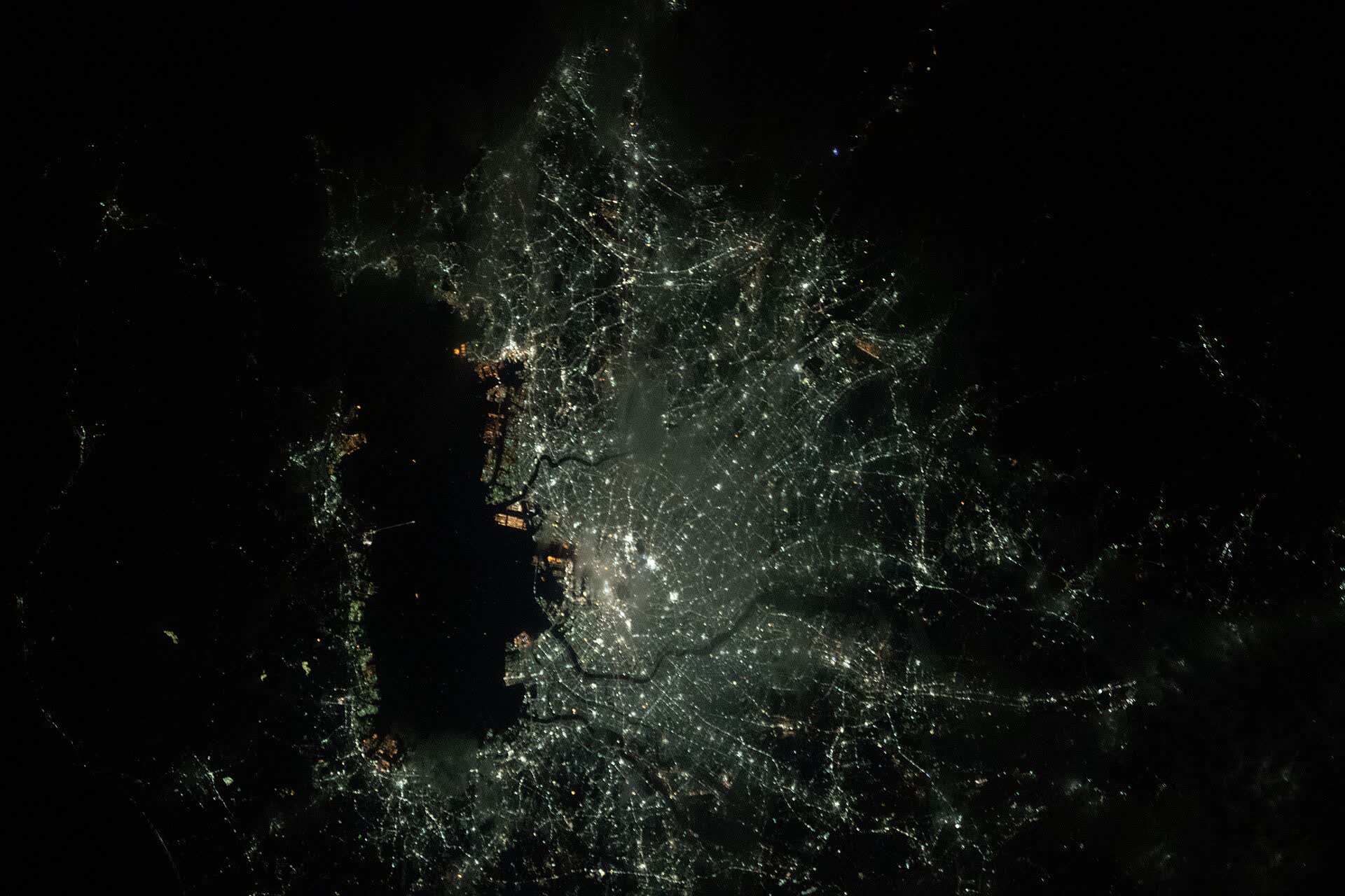 Tokyo, Kawasaki and Yokohama glowing around the dark water of Tokyo Bay at night