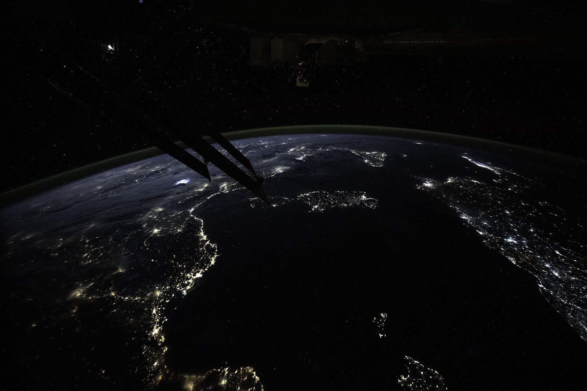 Coastal cities lit along the dark Mediterranean at night, the station’s structure in the foreground