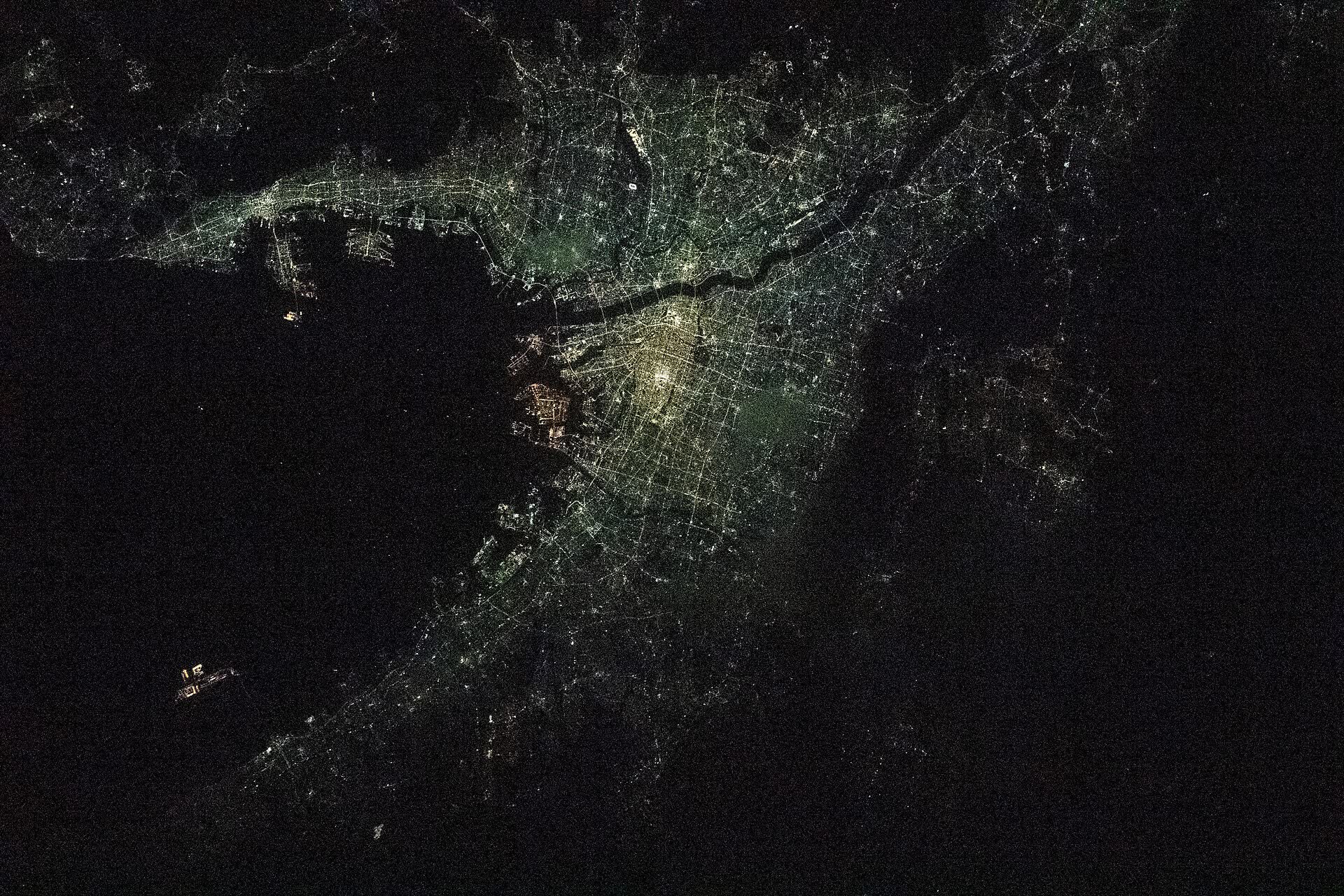 The lights of Osaka and Kobe curving around the dark water of Osaka Bay at night