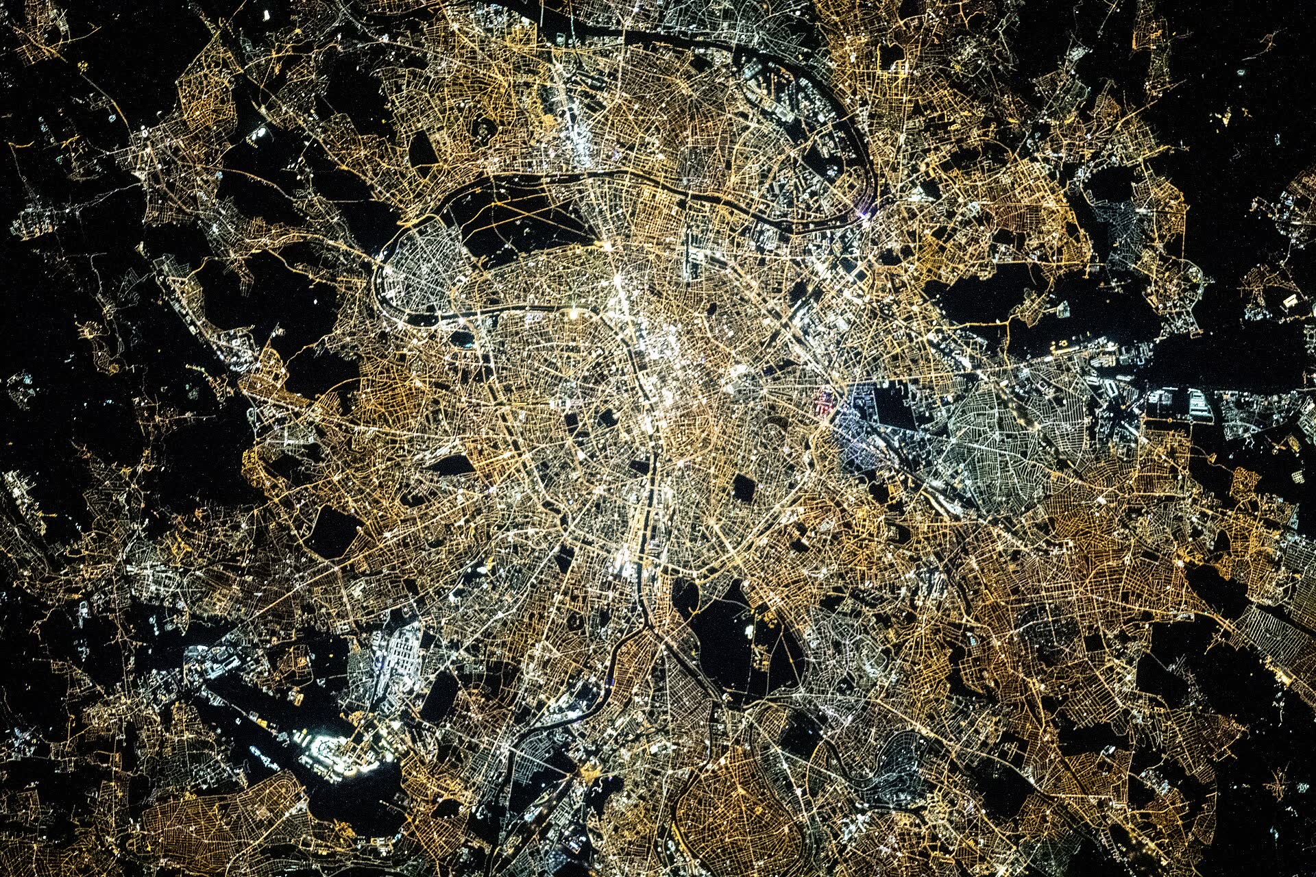 Paris at night in amber and white light, with the Seine winding through it
