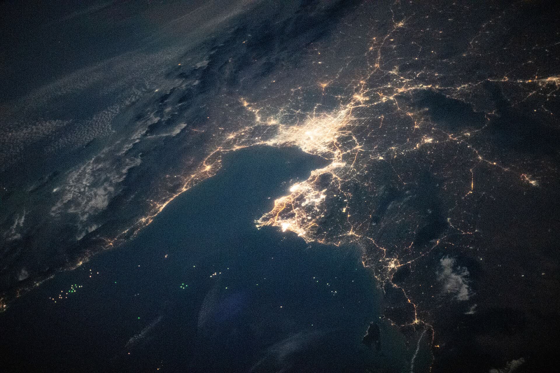 Bangkok's lights spreading inland from the Gulf of Thailand under thin cloud at night