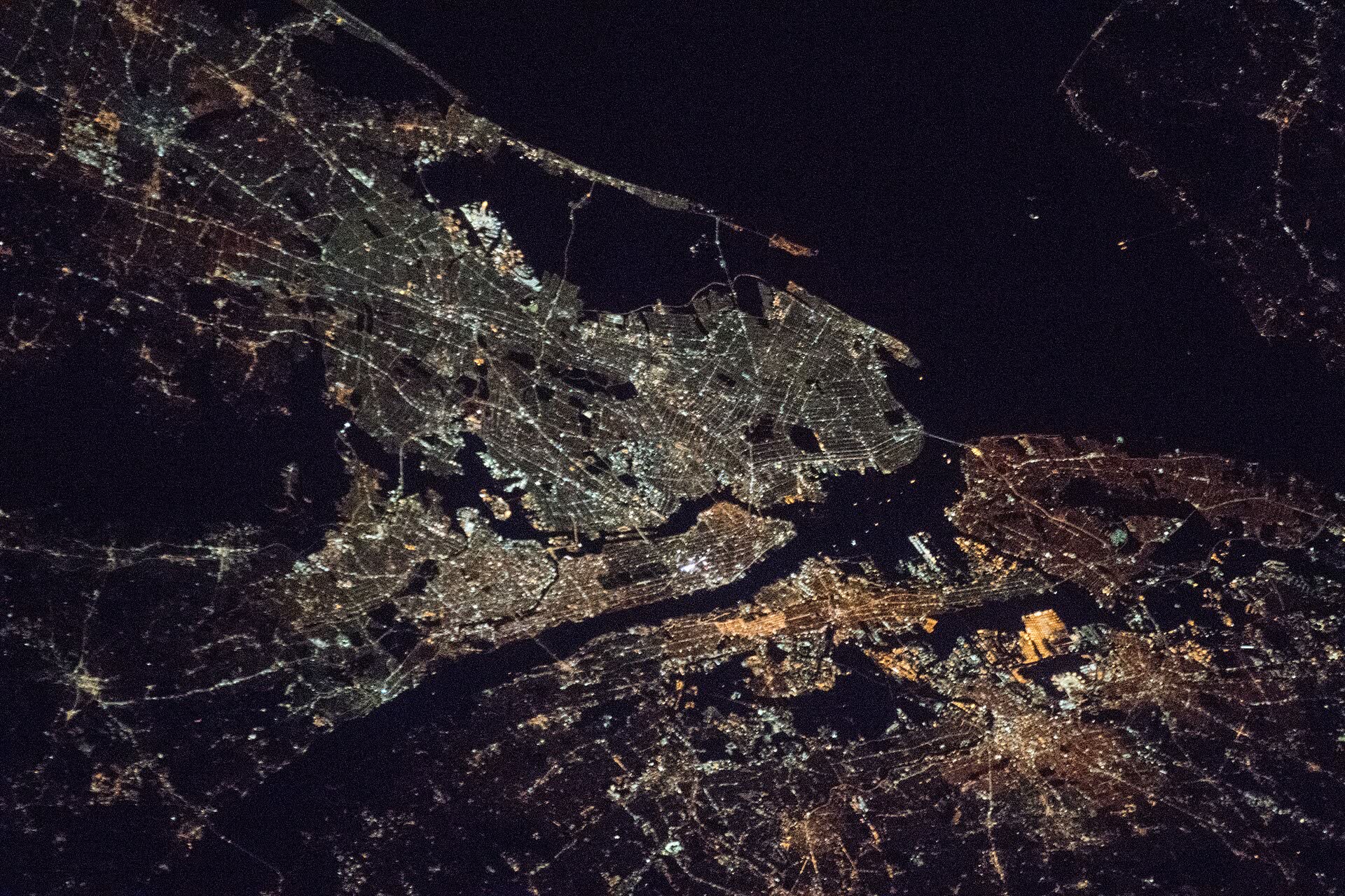 New York City and its rivers traced in white and amber lights at night